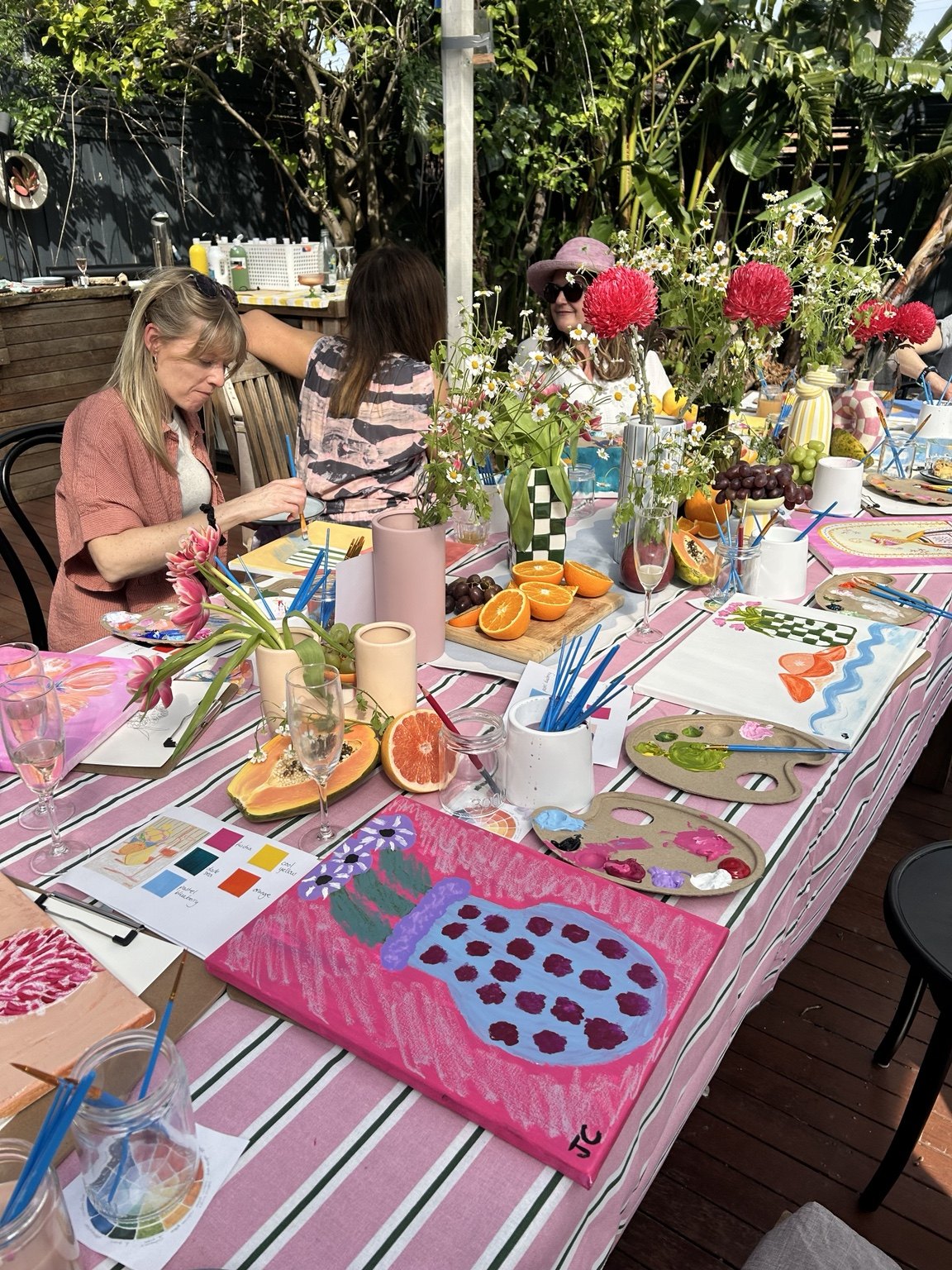 Friends painting together around a colourful outdoor workshop table