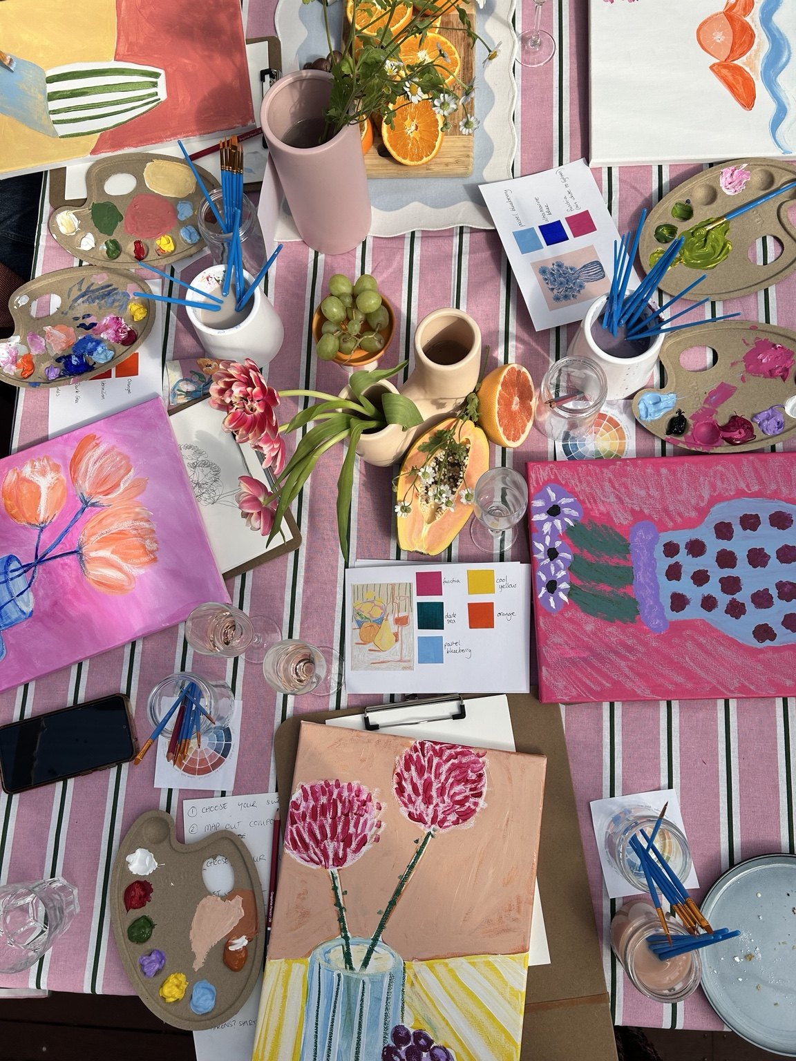 Finished colourful paintings, palettes and brushes spread across the workshop table